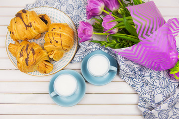 three croissants, two cups of coffee on the table and a bouquet of beautiful tulips