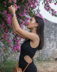 Asian girl. Beautiful Balinese women in black dress collects pink flowers in beautiful garden