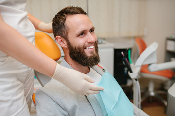 Obraz premium Сheerful handsome bearded man smiling to the camera sitting in a dental chair. Dentist and patient in dentist office. Amazing smile!