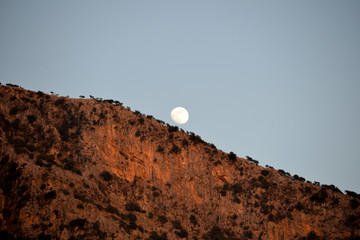 A full moon rises over the mountains. Evening sky