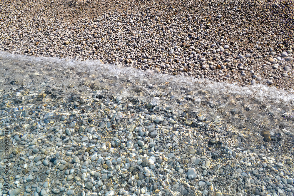 Wall mural Sea wave moves to a pebble beach. Summer sunny day. View from above