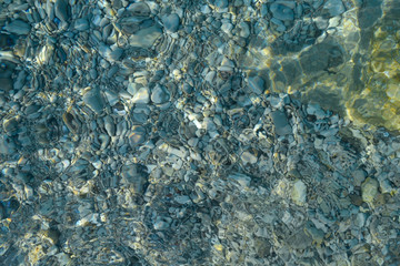 Beautiful colorful pebbles and big stone under turquoise blue clear water, scenic marine background or texture, top view