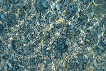 Obraz premium Beautiful colorful pebbles and big stone under turquoise blue clear water, scenic marine background or texture, top view