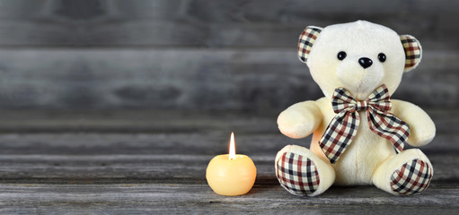 Teddy bear and white candle on wooden background with copy space