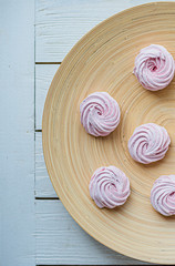 Merengue Marshmallow Zephyr lined in a circle on a bamboo plate on a white wooden background. Flat lay. Top view. Pink sweet homemade zephyr or marshmallow.