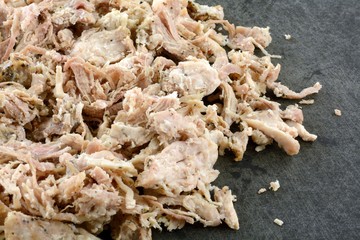 Cold cooked pulled pork meat on black cutting board ready to be reheated