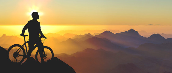 Cyclist in shorts and jersey on a modern carbon hardtail bike with an air suspension fork rides off-road on the orange-red hills at sunset evening in summer	