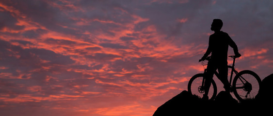 Cyclist in shorts and jersey on a modern carbon hardtail bike with an air suspension fork rides off-road on the orange-red hills at sunset evening in summer	