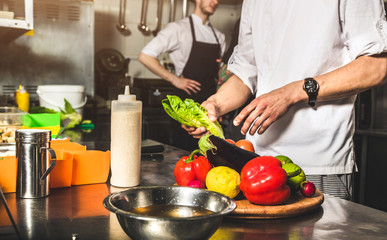 Professional chef cooking in the kitchen restaurant at the hotel, preparing dinner. A cook in an apron makes a salad of vegetables and pizza.