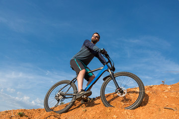 Fototapeta na wymiar Cyclist in shorts and jersey on a modern carbon hardtail bike with an air suspension fork rides off-road on the orange-red hills at sunset evening in summer
