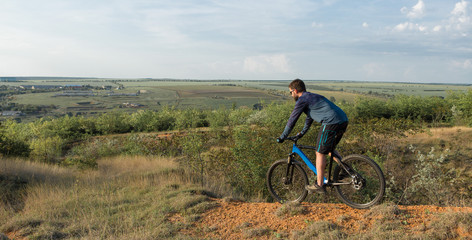 Naklejka na ściany i meble Cyclist in shorts and jersey on a modern carbon hardtail bike with an air suspension fork rides off-road on the orange-red hills at sunset evening in summer