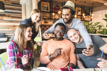 A company of multicultural  young people in a cafe eating pizza, drinking cocktails, having fun