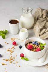White ceramic bowl of homemade granola with milk, fresh berries (blueberry and raspberry) and milk. Healthy breakfast ingredients. 