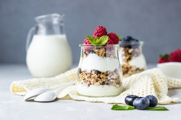 Jars with tasty parfait made of granola, berries and yogurt on stone grey table. Copy space.