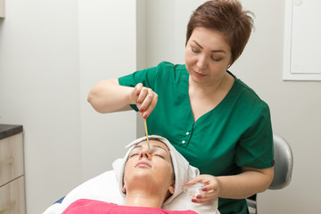 Obraz na płótnie Canvas Face skin care. Beautician applying beauty oil mask on face using brush In spa salon 