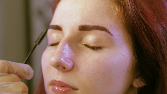 Beautician combs the client eyebrows after painting with a brush