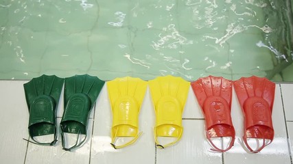 Diving fins in three different colors at the edge of the pool. Green yellow red color. Fins made of rubber and plasmass for swimming on a background of water.