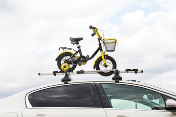Bicycle transportation - a children's bicycle on the roof of a car against the sky in a special mount for cycling. The decision to transport large loads and travel by car