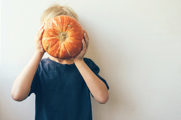 A blond boy holds an orange ripe pumpkin in front of him, hides his face. Funny children's joke....
