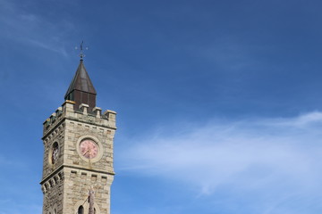 Fototapeta na wymiar Clock tower with red clock against a blue cloudy sky 