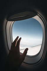 Porthole window in the plane with a man's hand during the flight.