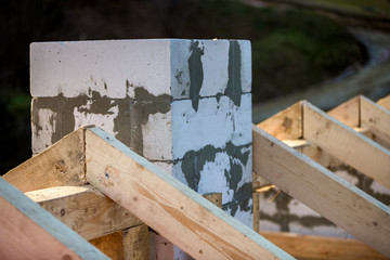 Close-up detail of roof frame of rough wooden lumber beams and chimney made of foam insulation blocks on blurred green background. Building, roofing, construction and renovation concept.