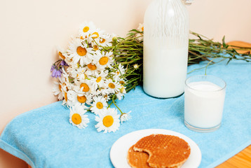 Simply stylish wooden kitchen with bottle of milk and glass on table, summer flowers camomile, healthy foog moring concept close up