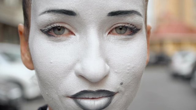 A mime girl in a black dress coat poses for the camera.
