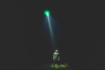 The UFO shines on a male standing on the grass. night time