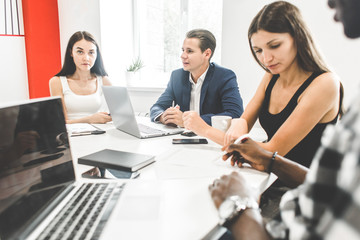 Fototapeta premium A team of young office workers, businessmen with laptop working at the table, communicating together in an office. Corporate businessteam and manager in a meeting. coworking.