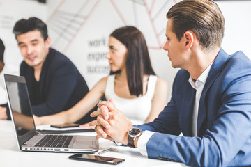 A team of young office workers, businessmen with laptop working at the table, communicating together in an office. Corporate businessteam and manager in a meeting. coworking.