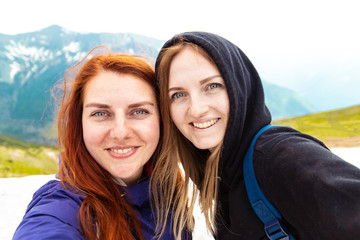 Two girls take a picture with their mobile. Two friends enjoy nature and the outdoors on the side of the mountain