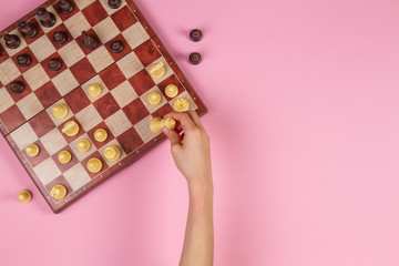 Kid hands over a chessboard playing chess game on pink background, top view
