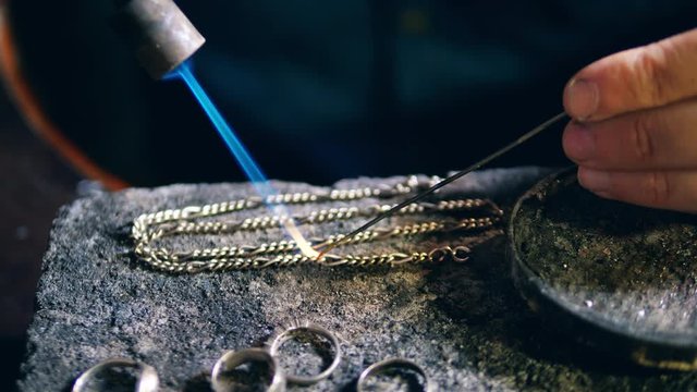 Jeweler, goldsmith in a professional jewelry workshop welds a metal chain at a jewellery shop.