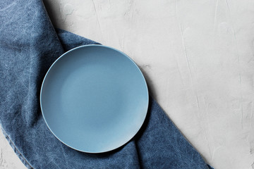 Light grey table with empty blue plate and denim napkin