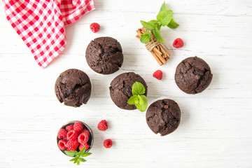 Chocolate muffins with raspberries and mint leaves on white wooden background, top view