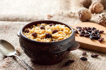 Sweet millet porridge with dark raisins in ceramic rustic bowl