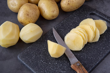Cooking.Slicing fresh potatoes into slices on a cutting Board,dark background.