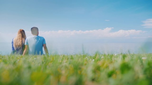 A young couple is sitting on a green lawn in a picturesque place near the lake