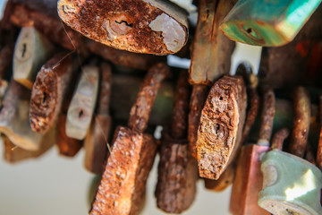 A detail of several old and rusty locks hanging on a handrail on a bridge. 