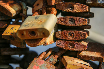 A detail of several old and rusty locks hanging on a handrail on a bridge. 
