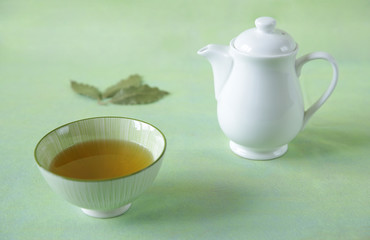 green tea in a bowl with a teapot and tea leaves on a light green surface. It is a rich source of antioxidants and polyphenols. A healthy drink for health and vitality.