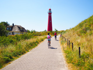 Back view cyclists traveling on the road heading towards to lighthouse in Schiermonnikoog islands,...