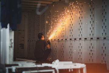 A worker inside an iron container polishes metal. Sparks fly from friction