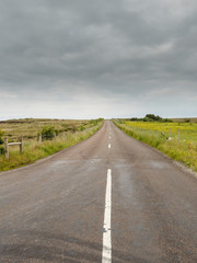 Old road in the country, Simple rural landscape, Cloudy sky. Green fields on each side.Old road in the country, Simple rural landscape, Cloudy sky. Green fields on each side. Vertical image.