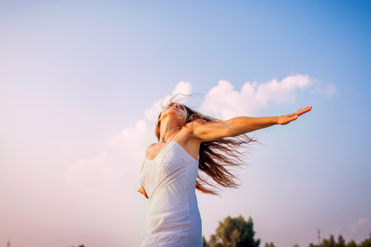 Young woman feeling free and happy raising arms and spinning around outdoors at sunset