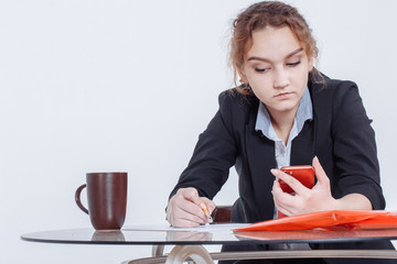 Portrait of young beautiful smiling casual woman sitting at office desk enjoying her cup of coffee while working or studying on laptop computer at small home office or in the student dorm. Indoors