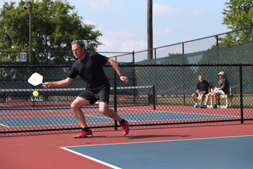 A senior athlete hits a shot, competing in singles, of a pickleball tournament.