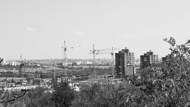 Several tower cranes build a multi-storey building and move cargo, long-range plan, time-lapse, monochrome