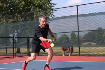 A senior athlete hits a shot, competing in singles, of a pickleball tournament.